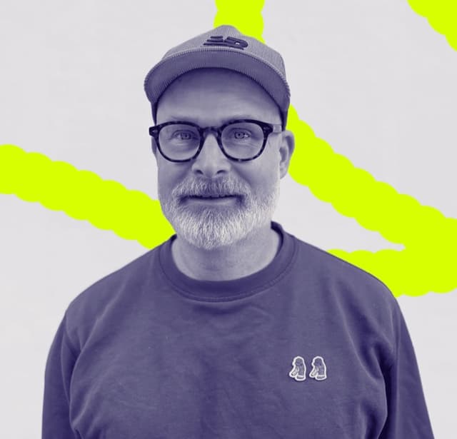 Dominik Heilig, wearing a cap and glasses, in front of a neon-yellow brushstroke